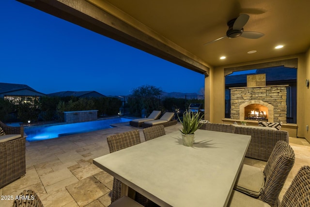 patio at twilight with an outdoor pool, a fenced backyard, ceiling fan, an outdoor stone fireplace, and outdoor dining space