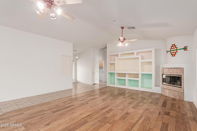 unfurnished living room featuring ceiling fan, lofted ceiling, a fireplace, wood finished floors, and visible vents