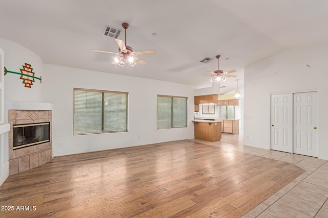 unfurnished living room with vaulted ceiling, a tiled fireplace, visible vents, and light wood-style floors