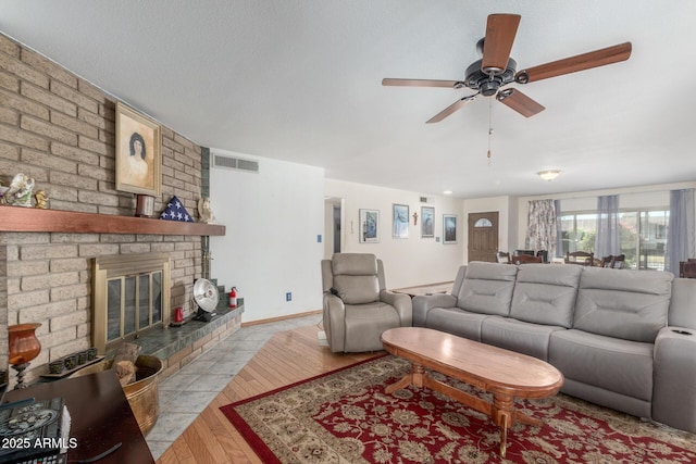 living room featuring ceiling fan, light hardwood / wood-style floors, a textured ceiling, and a brick fireplace