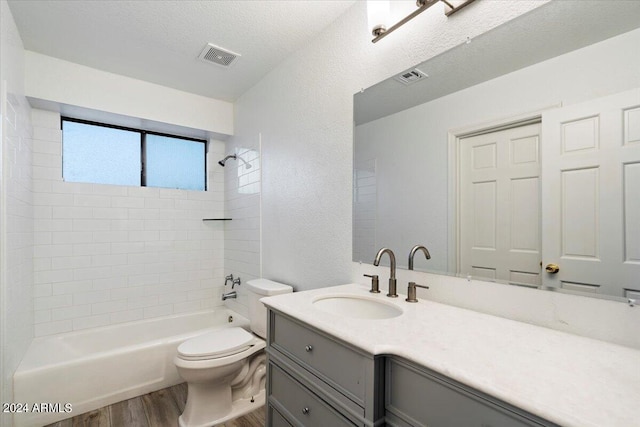 full bathroom featuring hardwood / wood-style flooring, a textured ceiling, vanity, toilet, and tiled shower / bath combo