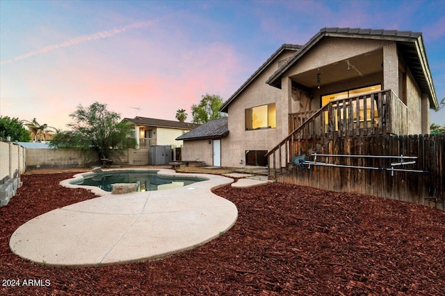 back house at dusk with a fenced in pool and a patio