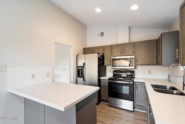 kitchen featuring stainless steel appliances, lofted ceiling, kitchen peninsula, sink, and backsplash