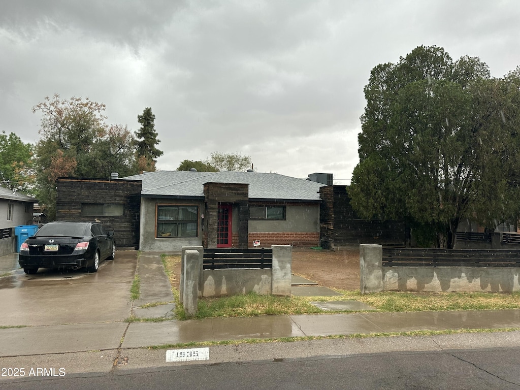 view of front of house with a fenced front yard, brick siding, roof with shingles, and driveway