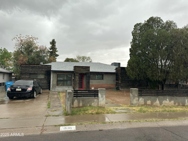 view of front of house with a fenced front yard, brick siding, roof with shingles, and driveway