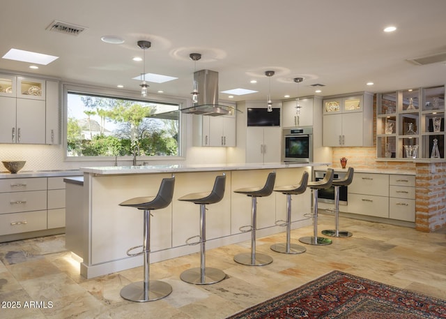 kitchen with a skylight, a large island, stainless steel oven, island exhaust hood, and decorative light fixtures