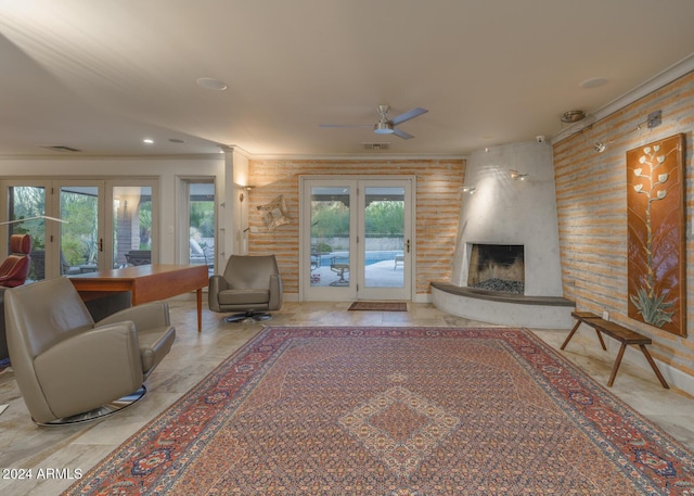 living room featuring french doors, rustic walls, ornamental molding, ceiling fan, and a fireplace