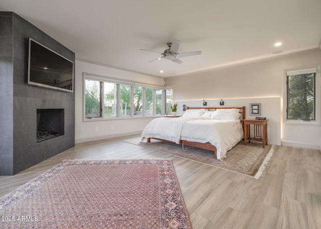 bedroom with a fireplace, light hardwood / wood-style flooring, ceiling fan, and crown molding