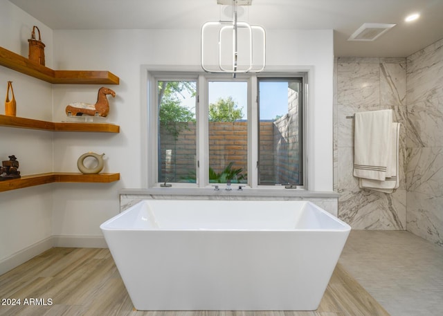 bathroom with a tub to relax in, an inviting chandelier, and hardwood / wood-style flooring