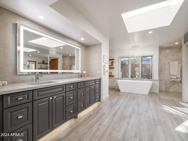 bathroom featuring a bathtub, vanity, a skylight, and tile walls