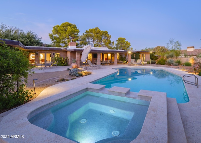 pool at dusk with an in ground hot tub and a patio