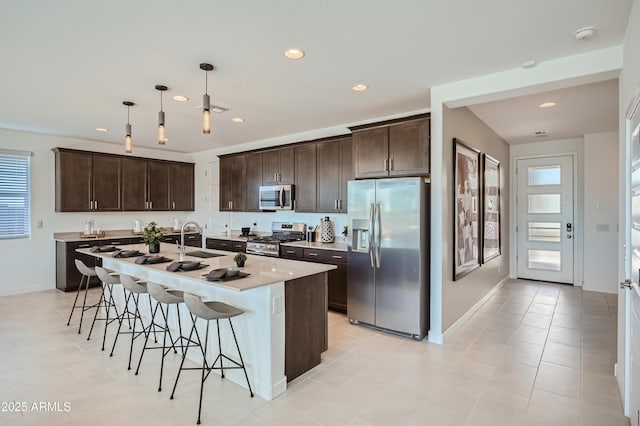 kitchen with pendant lighting, light countertops, appliances with stainless steel finishes, a kitchen island with sink, and a sink