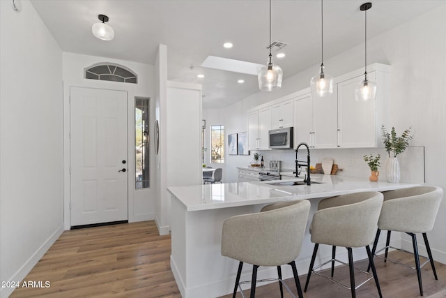 kitchen featuring sink, a kitchen breakfast bar, kitchen peninsula, decorative light fixtures, and white cabinets