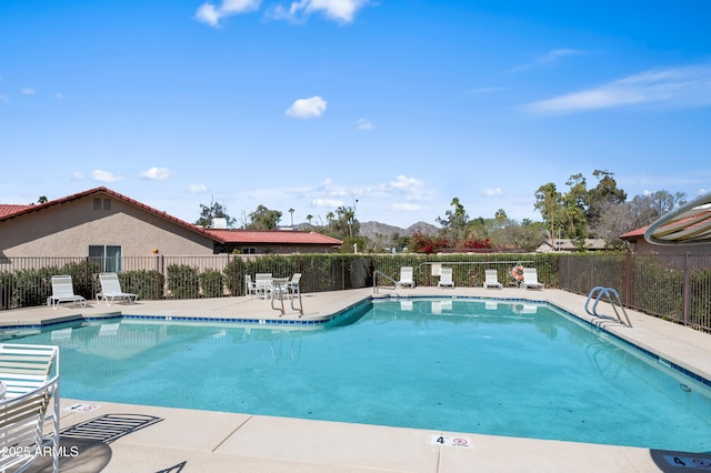 community pool with a patio, fence, and a mountain view