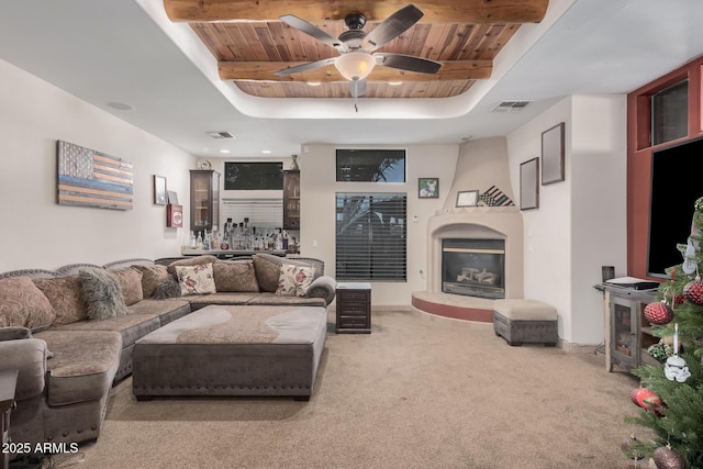 carpeted living room featuring a fireplace, beam ceiling, ceiling fan, and wooden ceiling