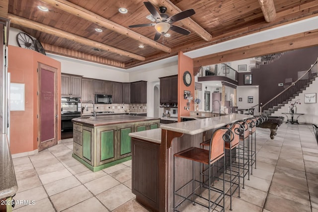 kitchen with a large island with sink, wooden ceiling, dark brown cabinetry, and black appliances