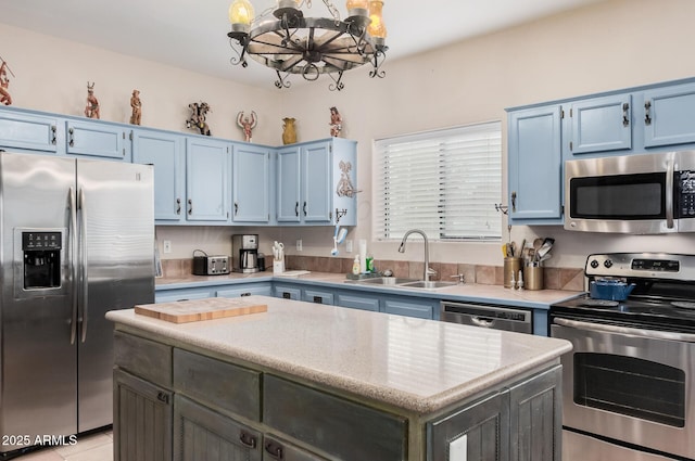 kitchen with sink, blue cabinets, a notable chandelier, a kitchen island, and appliances with stainless steel finishes