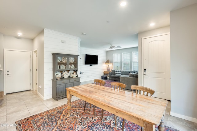 dining space with light tile patterned flooring, ceiling fan, and wood walls