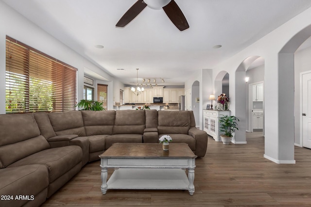 living area featuring arched walkways, ceiling fan with notable chandelier, wood finished floors, baseboards, and rail lighting