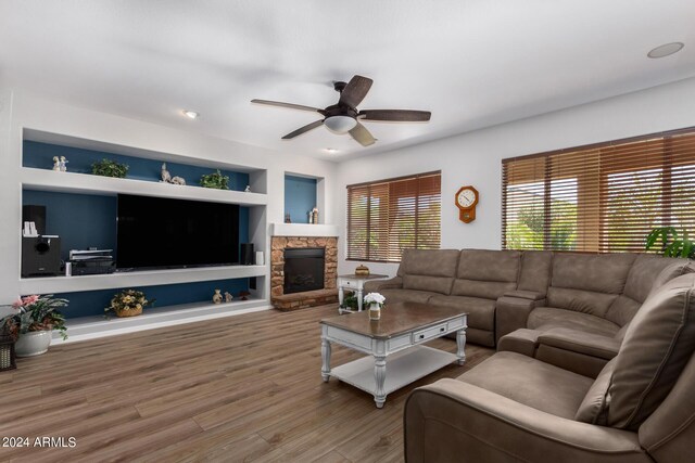 living room featuring ceiling fan, a fireplace, wood finished floors, and built in features