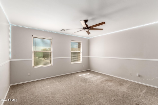 carpeted spare room with ceiling fan, baseboards, visible vents, and crown molding