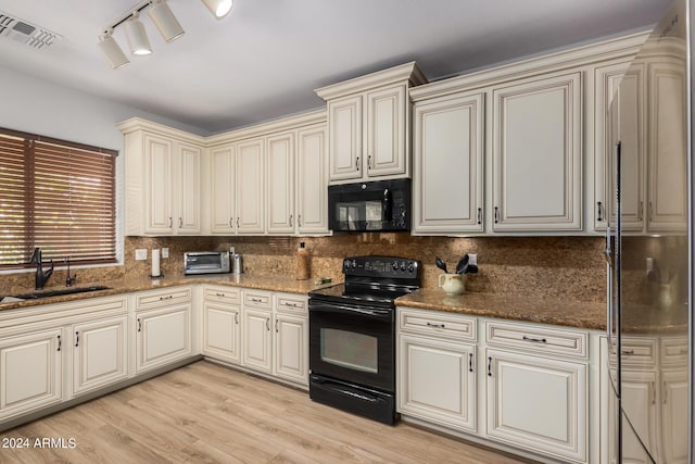 kitchen featuring visible vents, dark stone countertops, cream cabinets, black appliances, and a sink