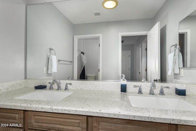 bathroom featuring toilet, double vanity, visible vents, and a sink