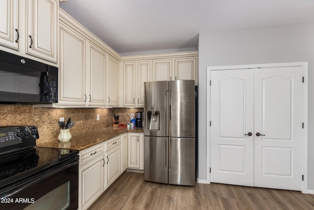 kitchen featuring cream cabinetry, decorative backsplash, dark stone counters, light wood-type flooring, and black appliances