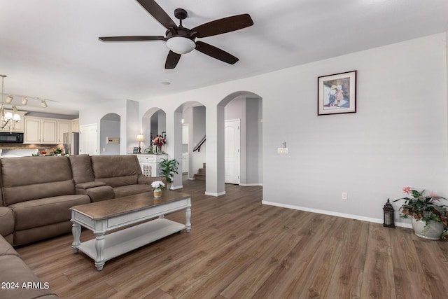 living room with arched walkways, ceiling fan with notable chandelier, wood finished floors, baseboards, and stairway