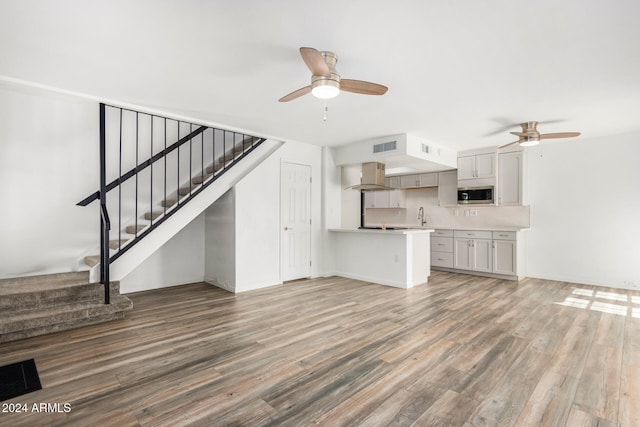 unfurnished living room featuring sink, wood-type flooring, and ceiling fan