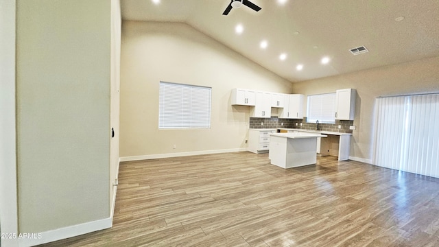 kitchen with ceiling fan, white cabinets, a kitchen island, decorative backsplash, and light wood-type flooring