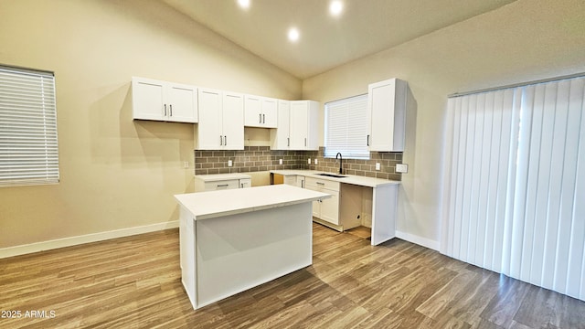 kitchen featuring a kitchen island, white cabinetry, sink, decorative backsplash, and light wood-type flooring