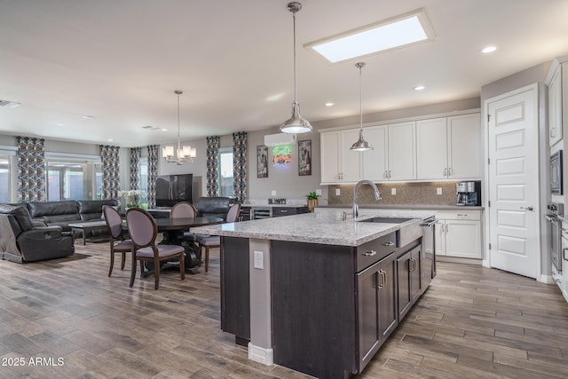 kitchen featuring light stone countertops, pendant lighting, an island with sink, white cabinetry, and dark brown cabinets