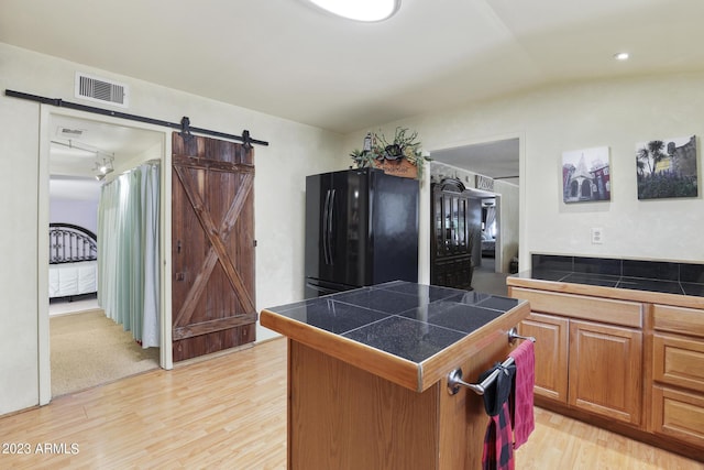 kitchen with visible vents, a kitchen island, freestanding refrigerator, a barn door, and light wood-style floors