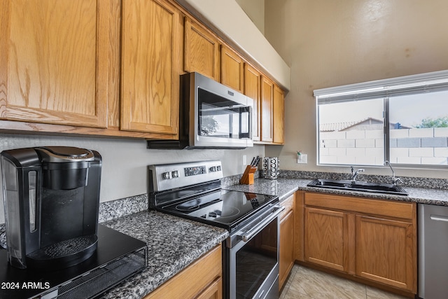 kitchen with dark stone counters, sink, light tile patterned floors, and stainless steel appliances