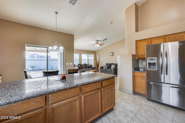 kitchen with stainless steel fridge, ceiling fan with notable chandelier, pendant lighting, dark stone countertops, and lofted ceiling