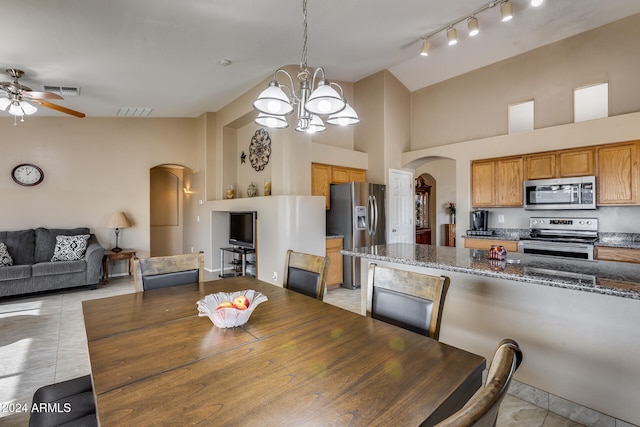 tiled dining room featuring ceiling fan with notable chandelier and high vaulted ceiling