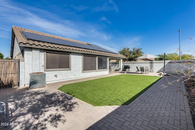 back of property with a lawn, solar panels, a patio area, and central AC