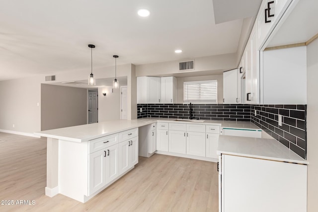 kitchen with visible vents, a peninsula, light wood-style floors, white cabinetry, and a sink