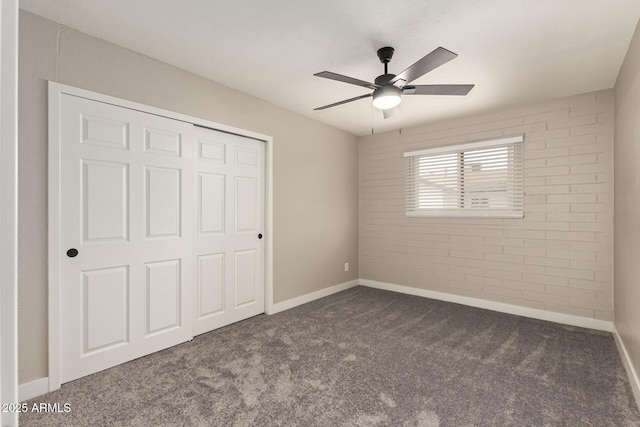 unfurnished bedroom featuring baseboards, a ceiling fan, brick wall, carpet flooring, and a closet