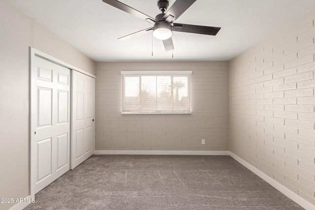 unfurnished bedroom featuring baseboards, brick wall, ceiling fan, carpet, and a closet