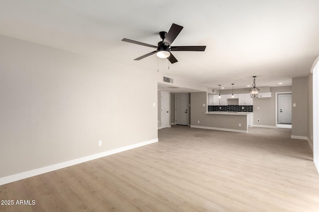 unfurnished living room featuring light wood-type flooring, visible vents, baseboards, and ceiling fan with notable chandelier