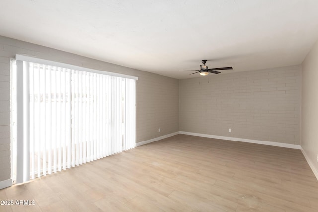 empty room with light wood-style floors, brick wall, baseboards, and ceiling fan