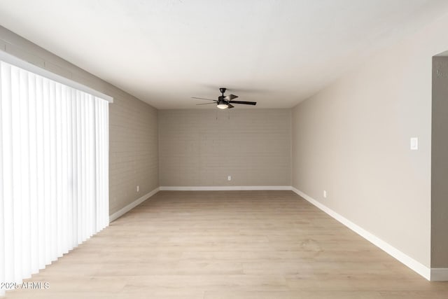 unfurnished room featuring light wood-style floors, baseboards, brick wall, and a ceiling fan