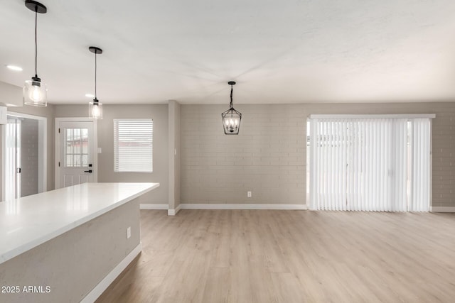 unfurnished dining area featuring brick wall, light wood-style flooring, and baseboards