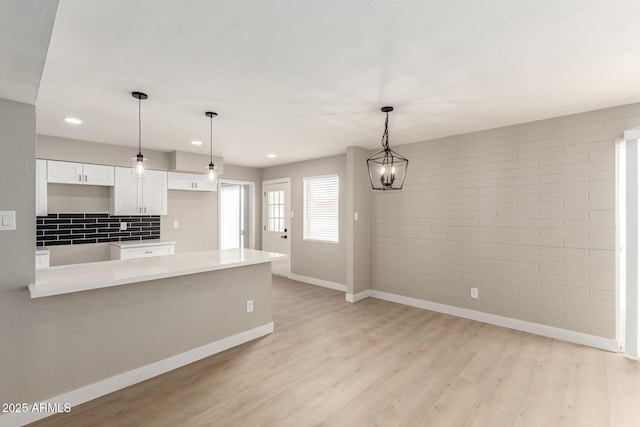 kitchen with hanging light fixtures, light wood-style floors, white cabinets, brick wall, and baseboards