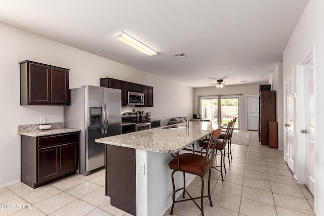 kitchen featuring sink, a breakfast bar area, stainless steel appliances, light stone counters, and an island with sink