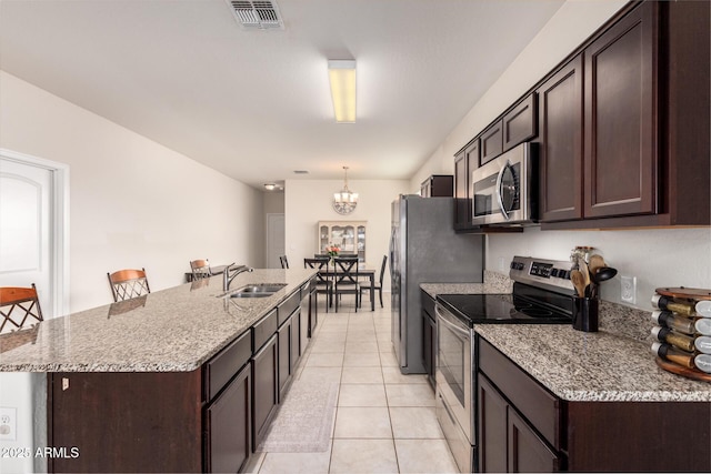 kitchen with appliances with stainless steel finishes, a breakfast bar, an island with sink, sink, and hanging light fixtures