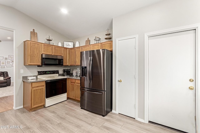 kitchen with stainless steel appliances, vaulted ceiling, and light wood-style flooring