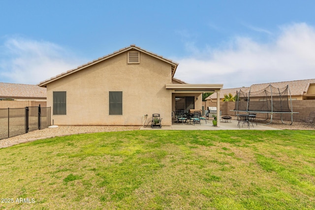 rear view of house featuring a fenced backyard, a lawn, stucco siding, a trampoline, and a patio area